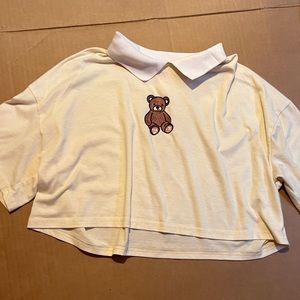 pastel yellow t-shirt with white collar and a brown bear on the front